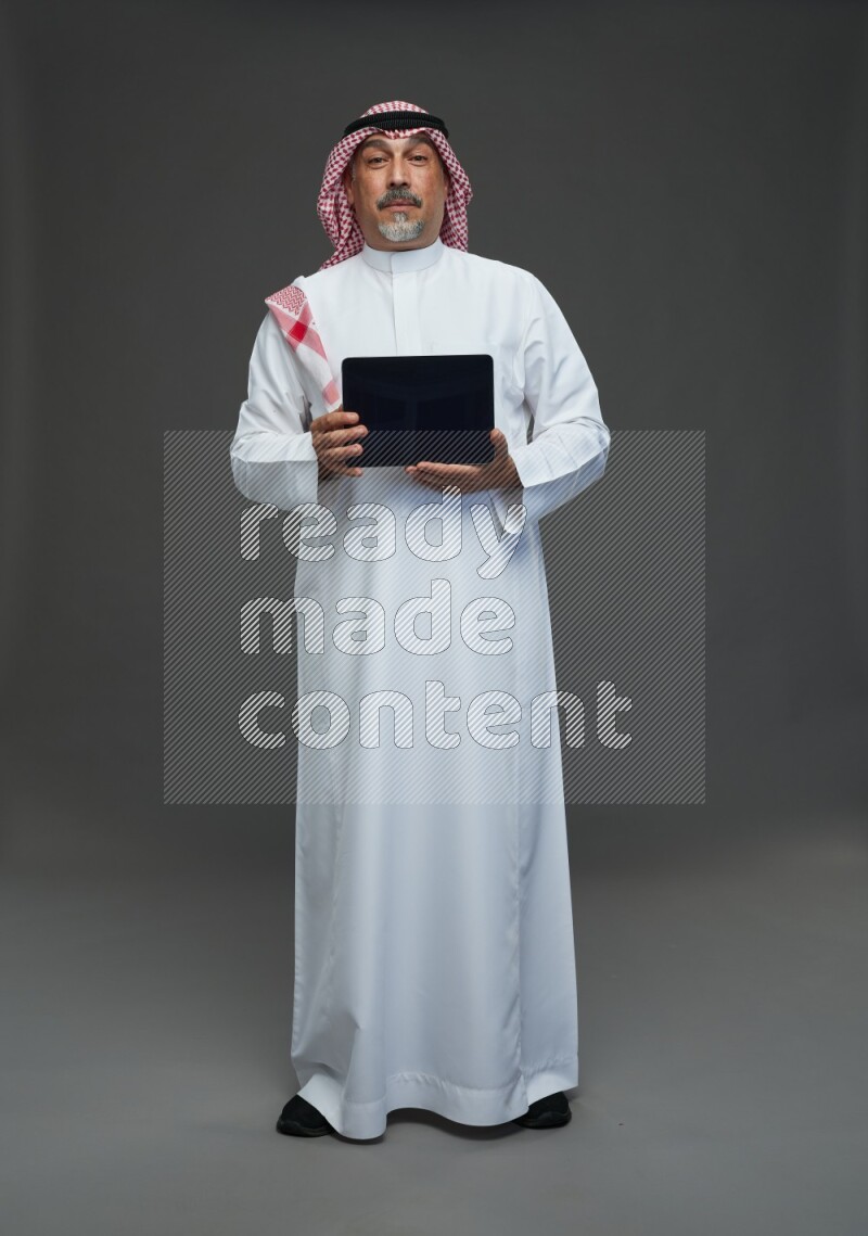 Saudi man with shomag Standing working on tablet on gray background
