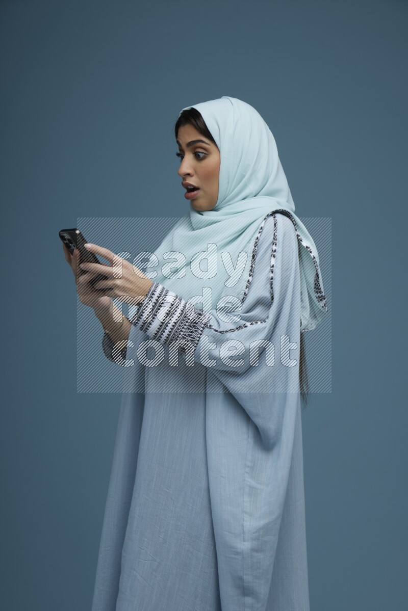A Saudi woman Texting in a blue background wearing a blue Abaya with hijab