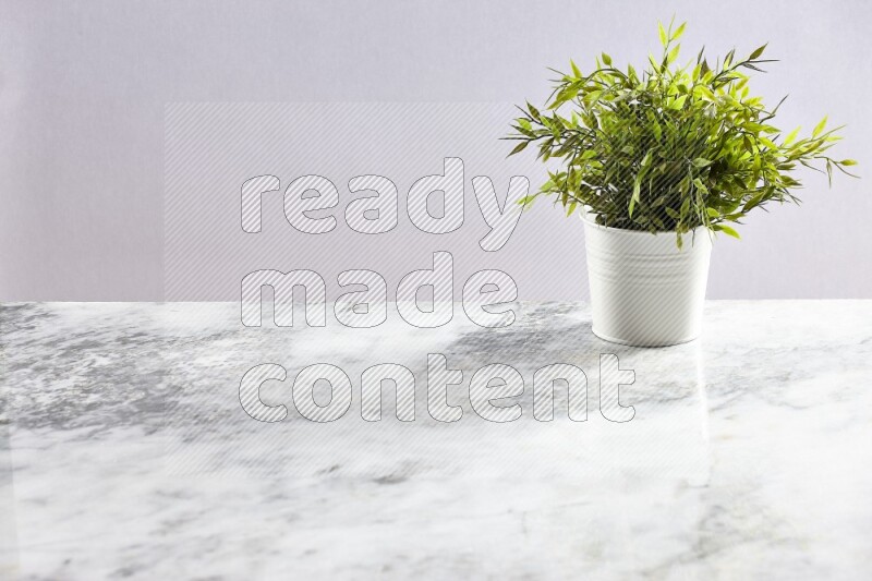 Green artificial plant in white pot on light grey marble background