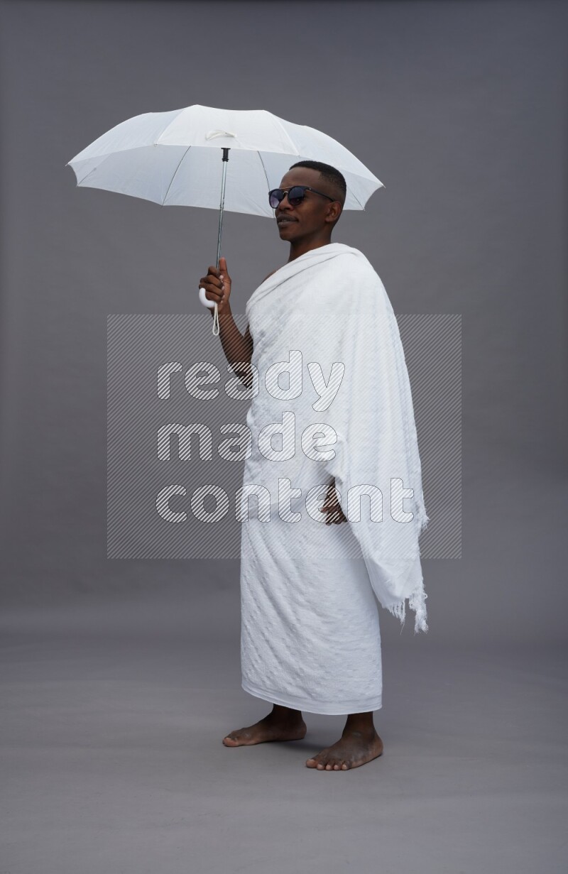 A man wearing Ehram Standing holding umbrella on gray background