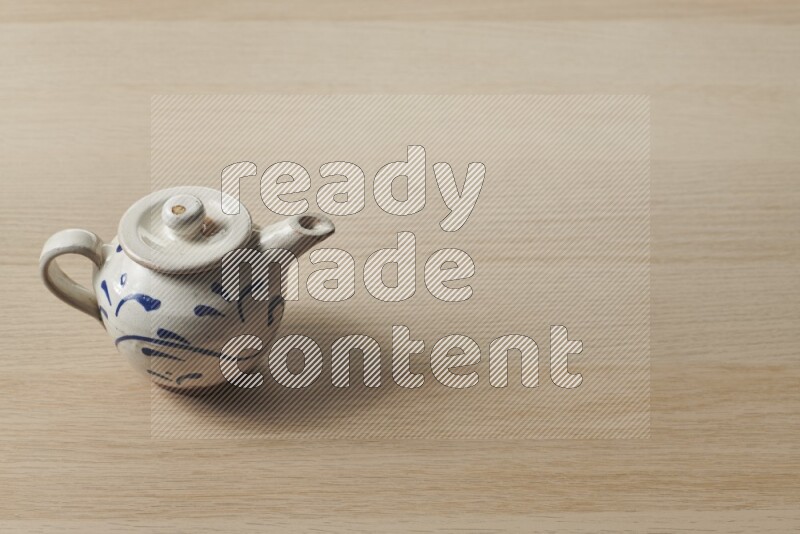A pottery teapot on light wooden background
