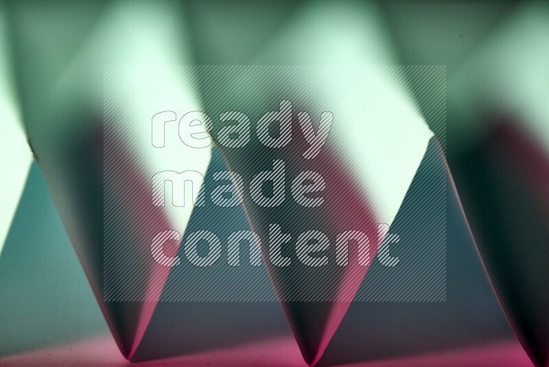 A close-up abstract image showing sharp geometric paper folds in green and pink gradients
