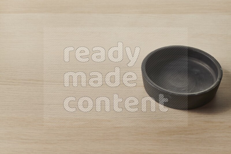 A black pottery bowl on light wooden background
