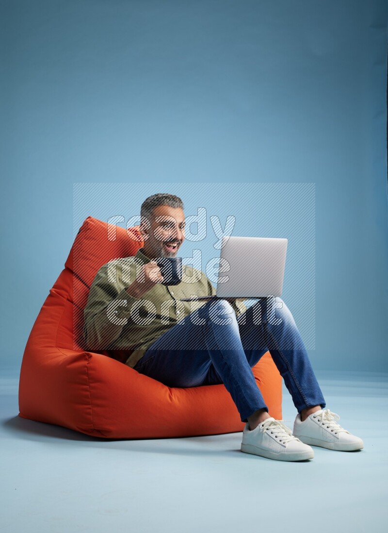 A man sitting on an orange beanbag and working on laptop