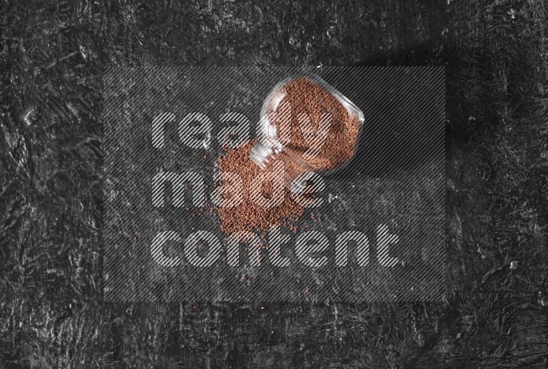 وعاء زجاجي مقلوب ممتلئ ببذور حب الرشاد وتناثرت البذور منه على أرضية سوداء