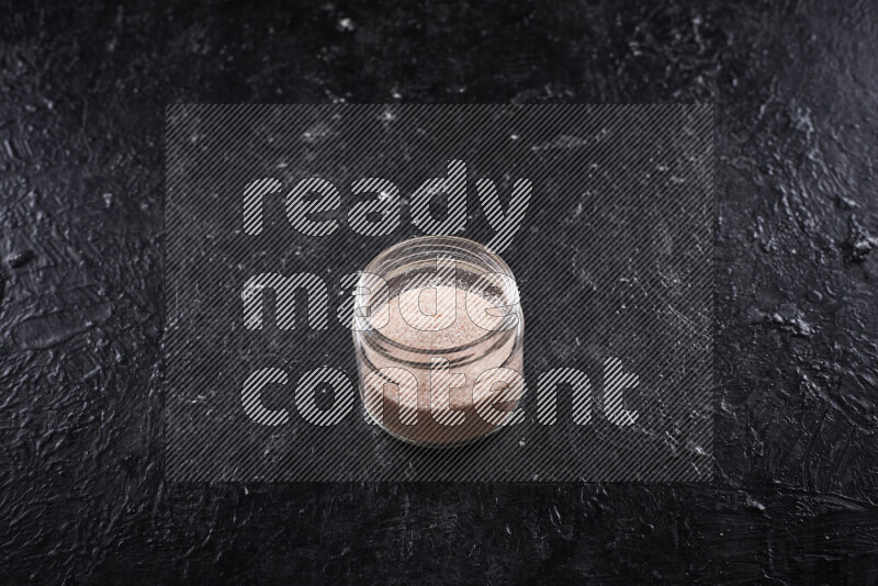 A glass jar full of fine himalayan salt on black background