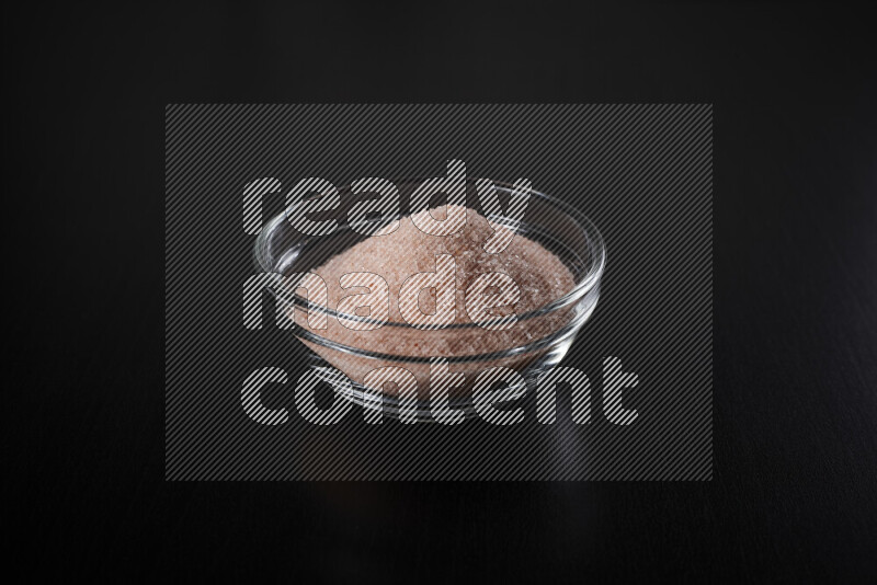 A glass bowl full of fine himalayan salt on black background