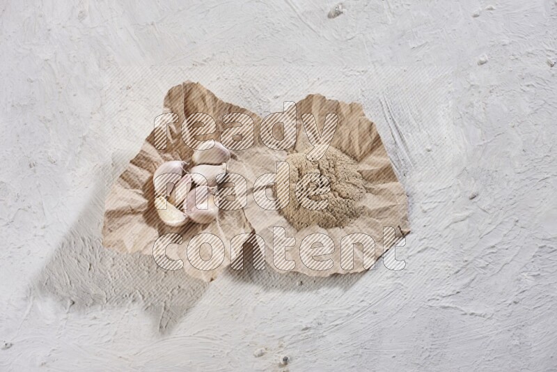 2 crumpled piece of paper full of garlic cloves and powder on a textured white flooring