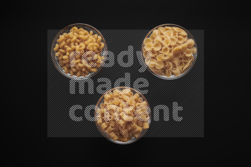 Different pasta types in glass bowls on black background