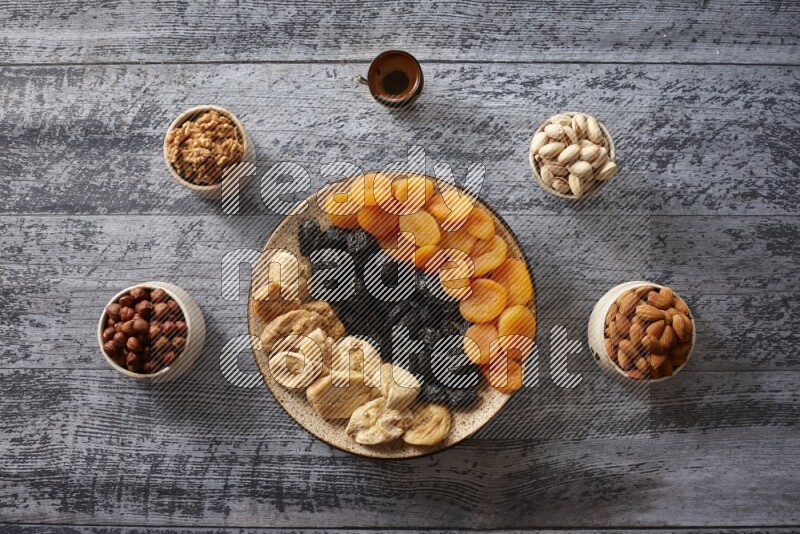 Dried fruits in a pottery plate with nuts and coffee in a dark setup