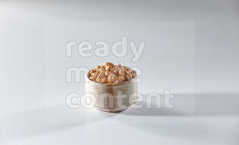 A beige ceramic bowl full of cashews on a white background in different angles