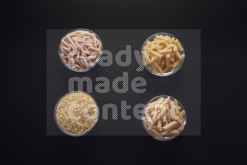 Different pasta types in glass bowls on black background