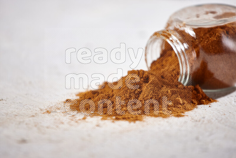 A glass jar full of ground paprika powder flipped with some spilling powder on white background