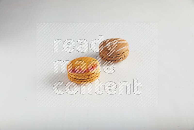 45º Shot of of two assorted Brown Irish Cream, and Orange Exotic macarons on white background