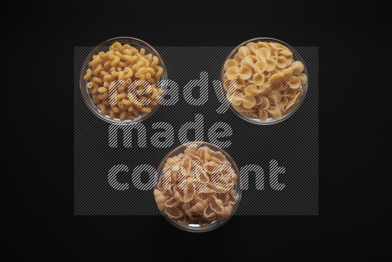 Different pasta types in glass bowls on black background