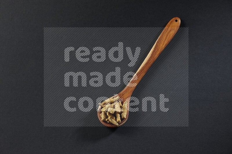 A wooden ladle full of dried turmeric fingers on black flooring