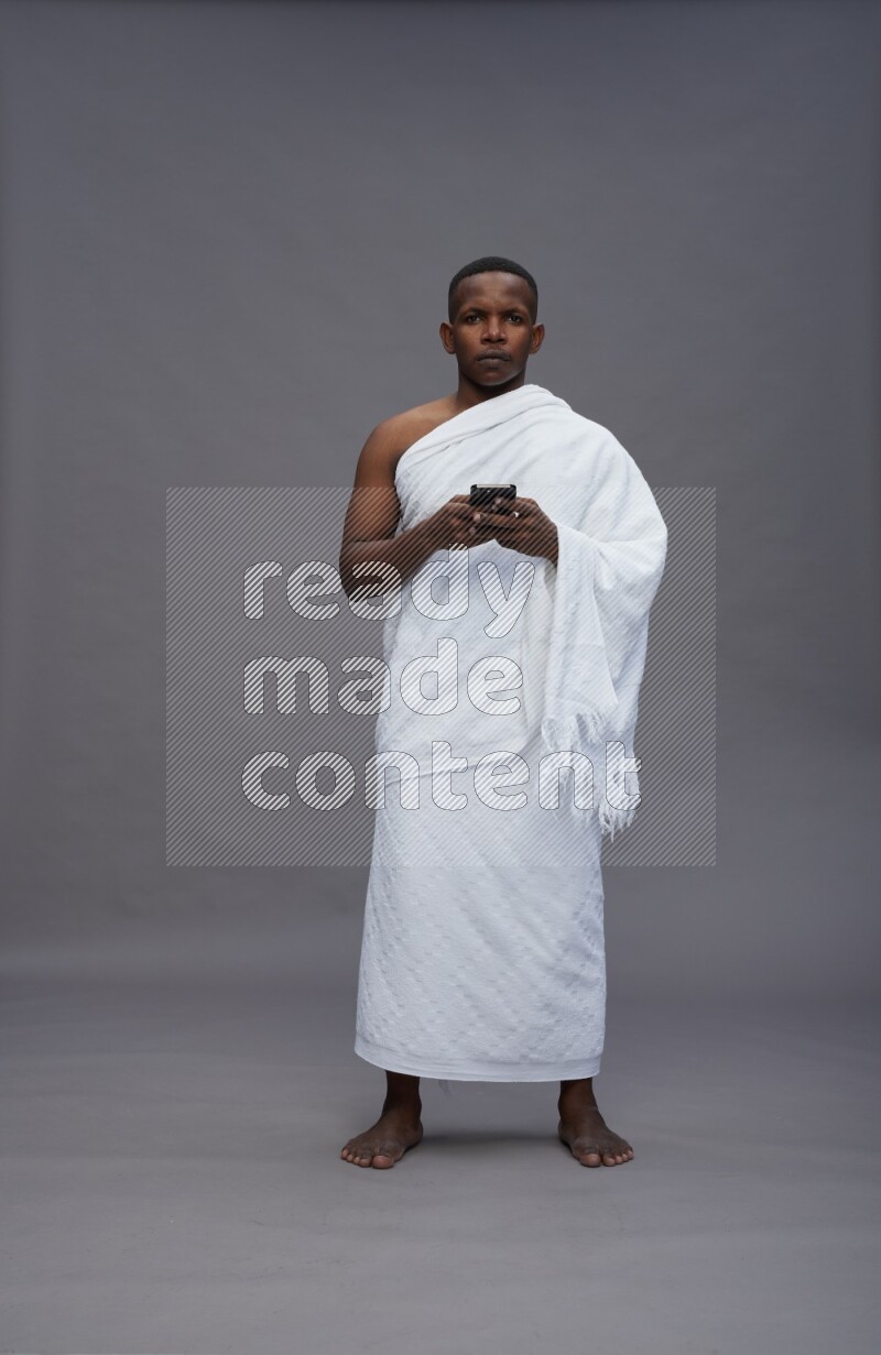 A man wearing Ehram Standing texting on phone on gray background