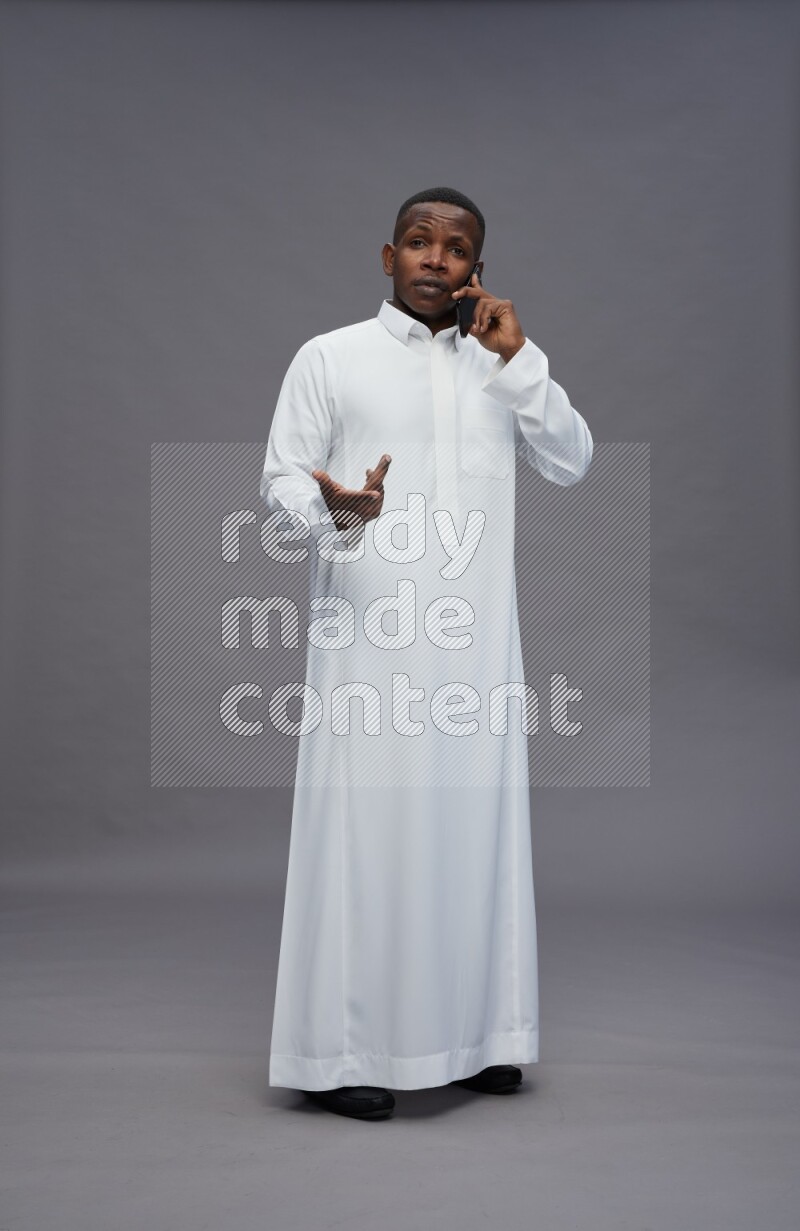Saudi man wearing thob standing talking on phone on gray background