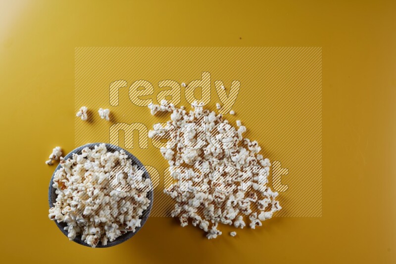 A multicolored pottery bowl full of popcorn with popcorn beside it on a yellow background in different angles