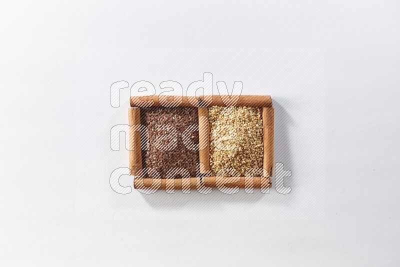 مربعان من أعواد القرفة ممتلئان ببذور الكتان وبذور السمسم علي خلفية بيضاء