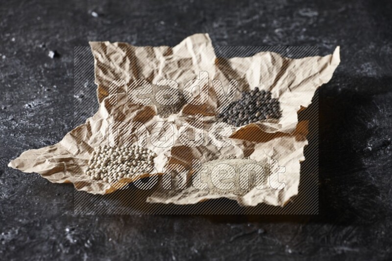 Crumpled pieces of paper full of black and white pepper beads and powder on a textured black flooring