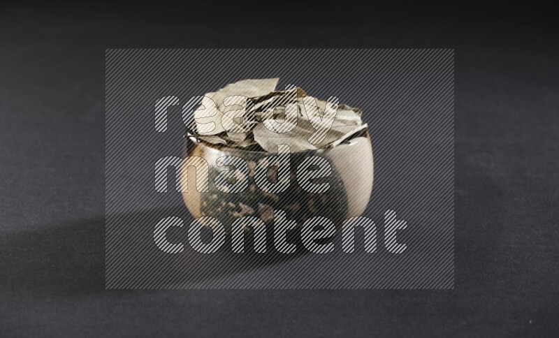A multicolored pottery bowl full of dried bay leaves on black flooring