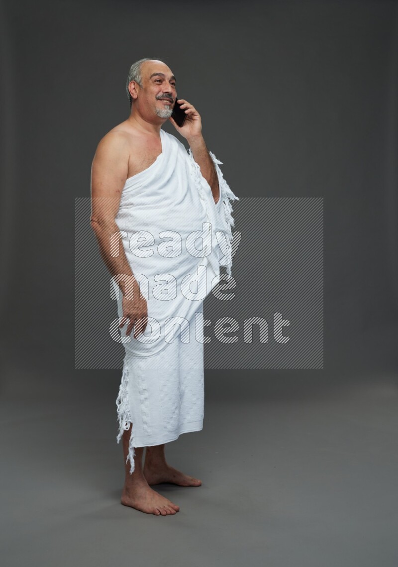 A man wearing Ehram Standing talking on phone on gray background