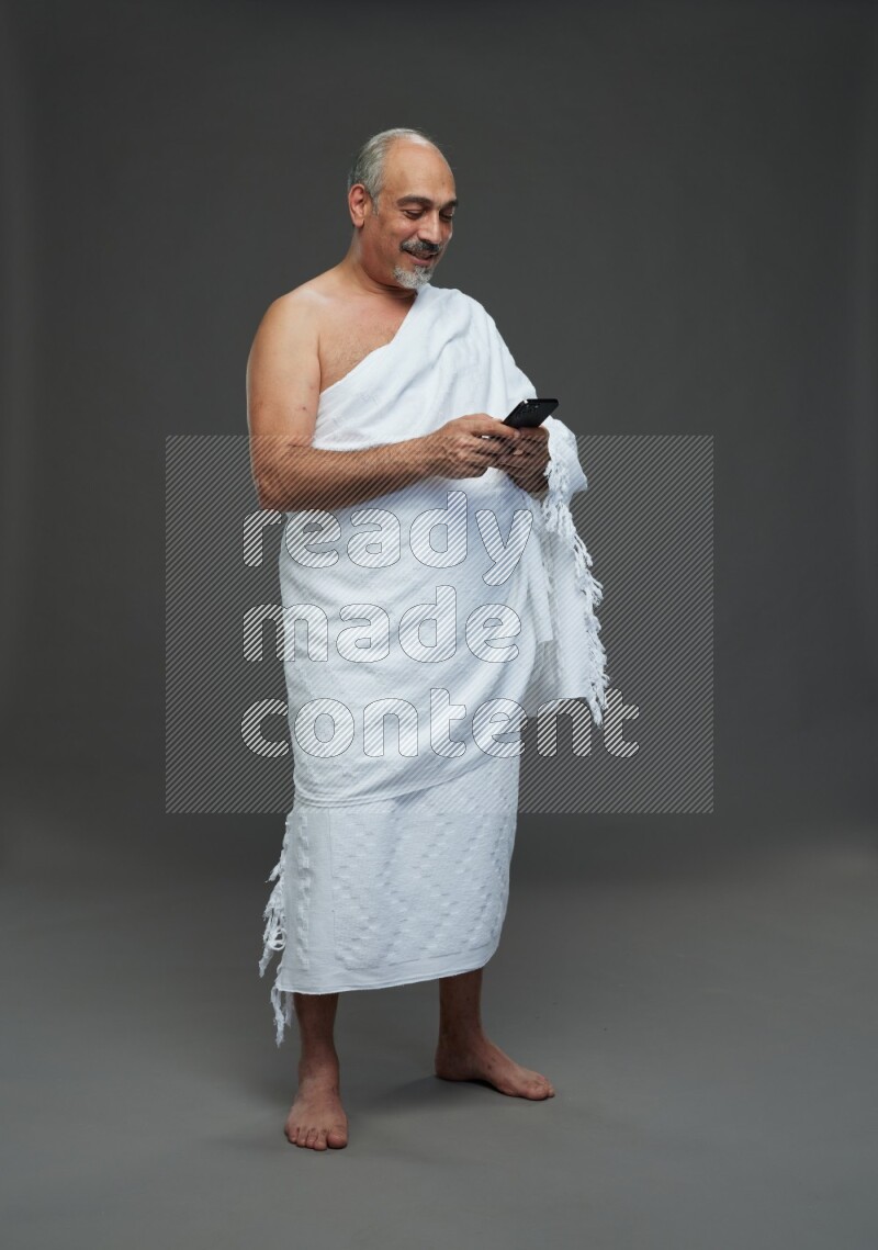 A man wearing Ehram Standing texting on phone on gray background