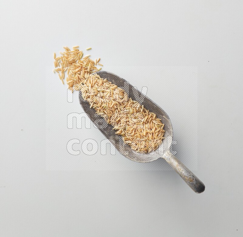Top-view of a long grain brown rice, and shovel on white background