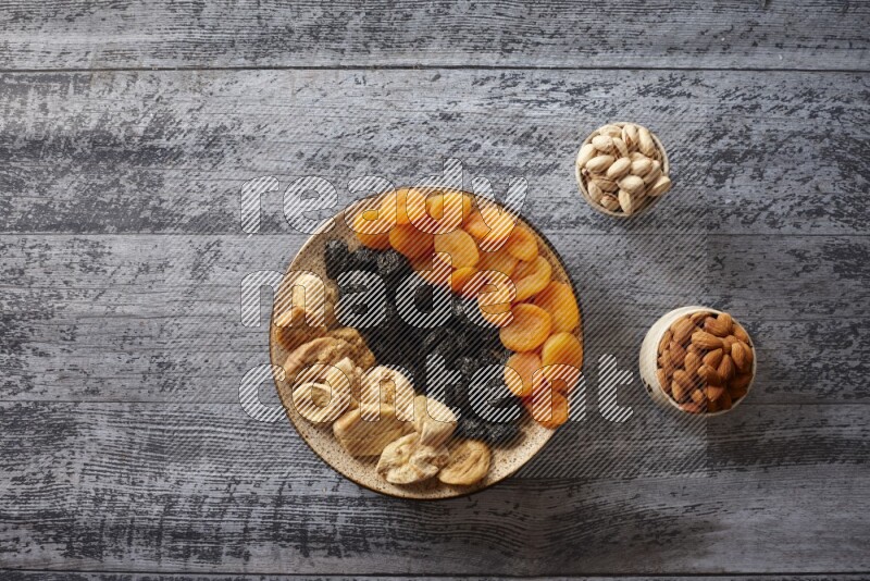 Dried fruits in a pottery plate with nuts and coffee in a dark setup