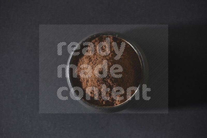 A black pottery bowl full of cloves powder on a black flooring