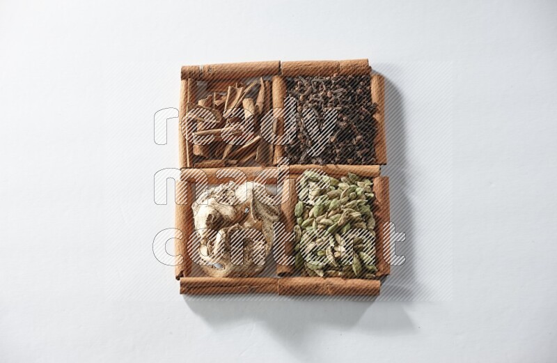 4 مربعات من أعواد القرفة ممتلئة بالهيل والقرفة والقرنفل والزنجبيل المجفف على أرضية بيضاء