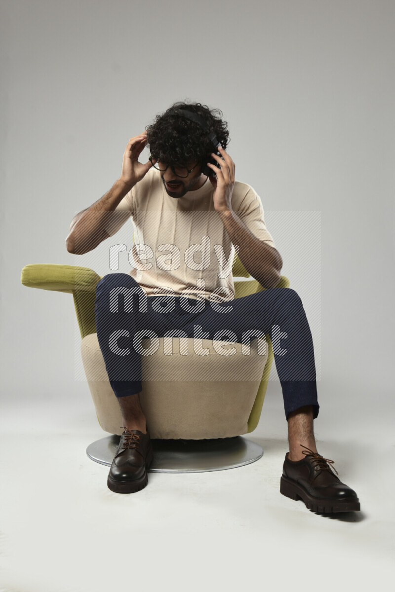 A man wearing casual sitting on a chair putting on headphones on white background