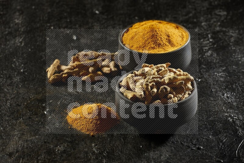 وعاءان من الفخار باللون الأسود، أحدهما ممتلئ ببودرة الكركم والآخر ممتلئ بأصابع كاملة من الكركم المجفف على خلفية سوداء