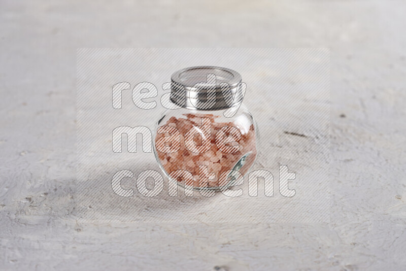 A glass jar full of coarse himalayan salt crystals on white background