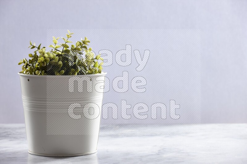 Green artificial plant in white pot on grey marble background