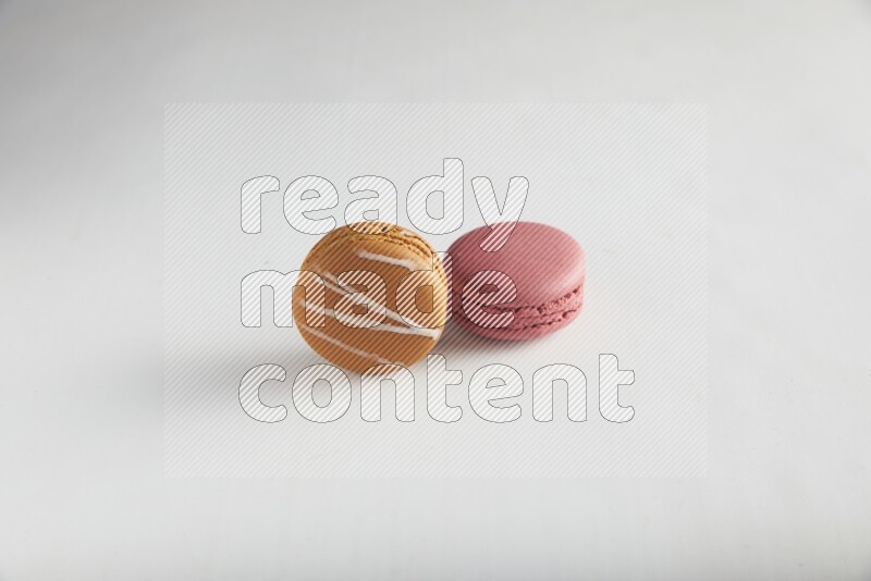 45º Shot of of two assorted Brown Irish Cream, and Pink Raspberry macarons on white background