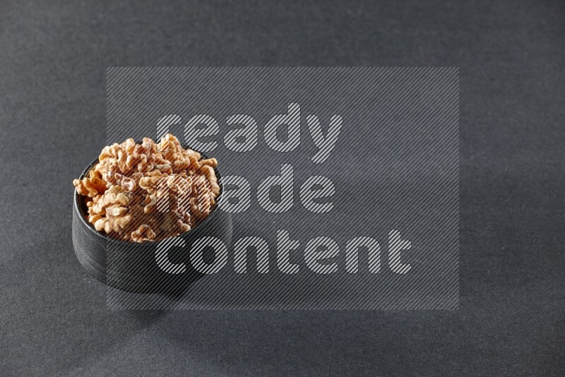 A black pottery bowl full of peeled walnuts on a black background in different angles