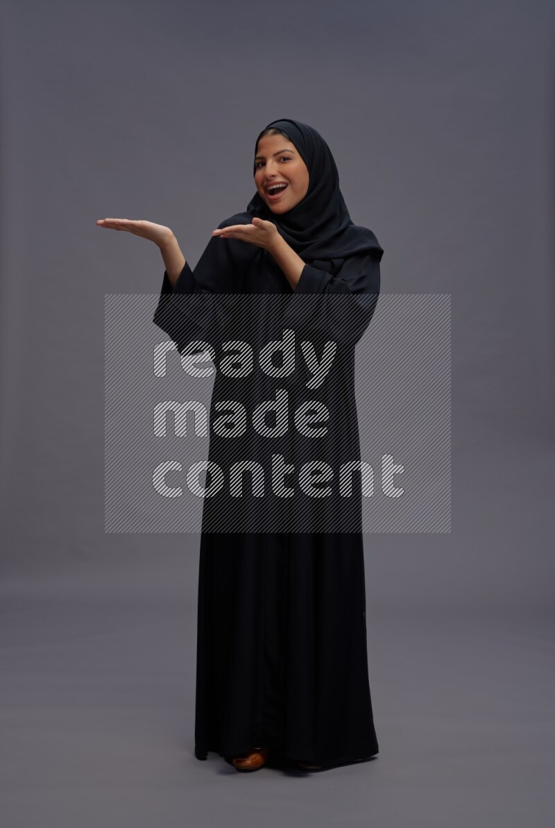 Saudi woman wearing Abaya standing interacting with the camera on gray background