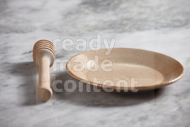 Beige pottery plate with wooden honey dipper on the side on grey marble background