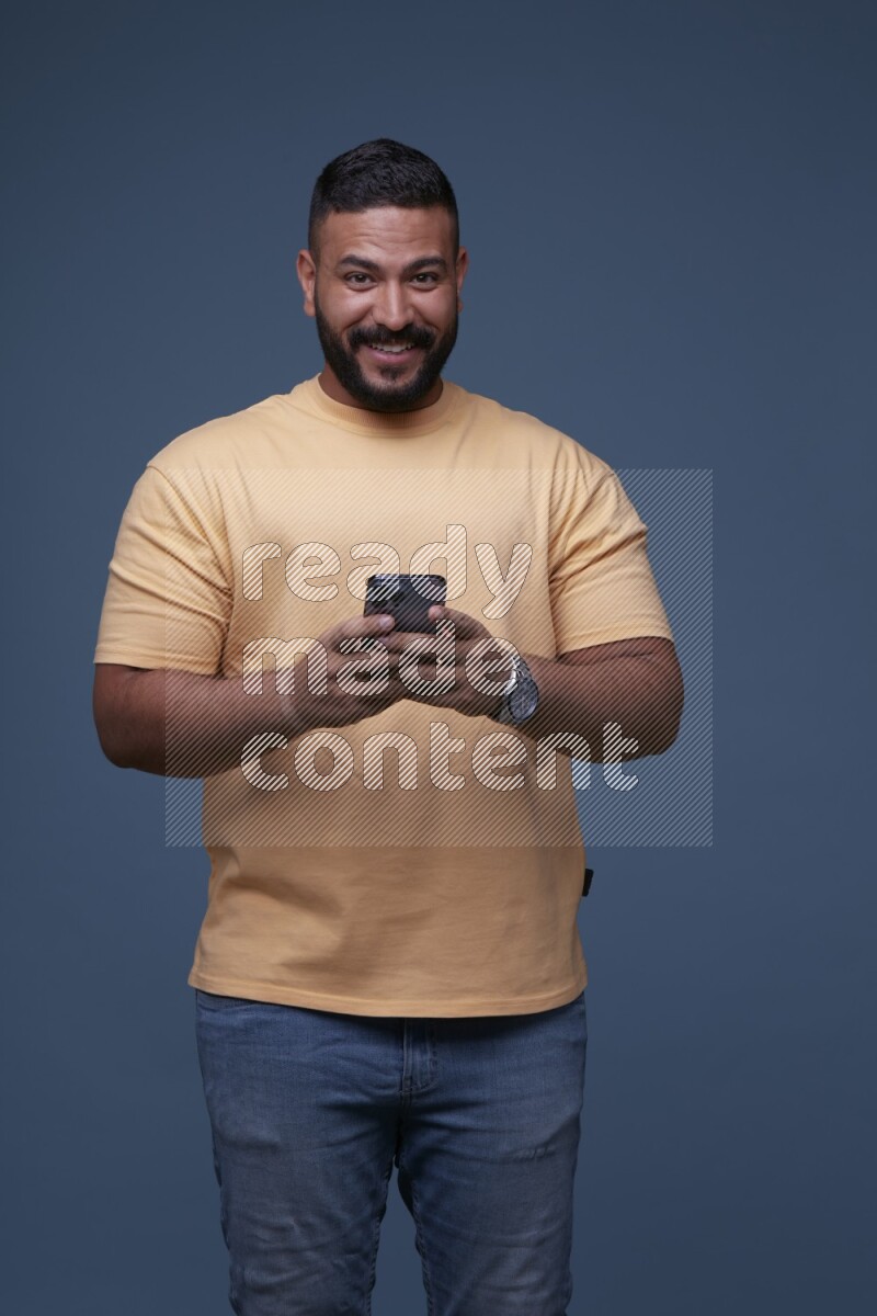 رجل يرتدي قميص اصفر وبنطال جينز ازرق يستخدم جواله