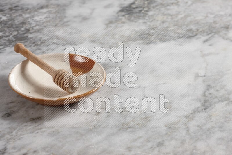 طبق فخاري متعدد الألوان مع ملعقة عسل خشبية بداخله على خلفية من الرخام الرمادي