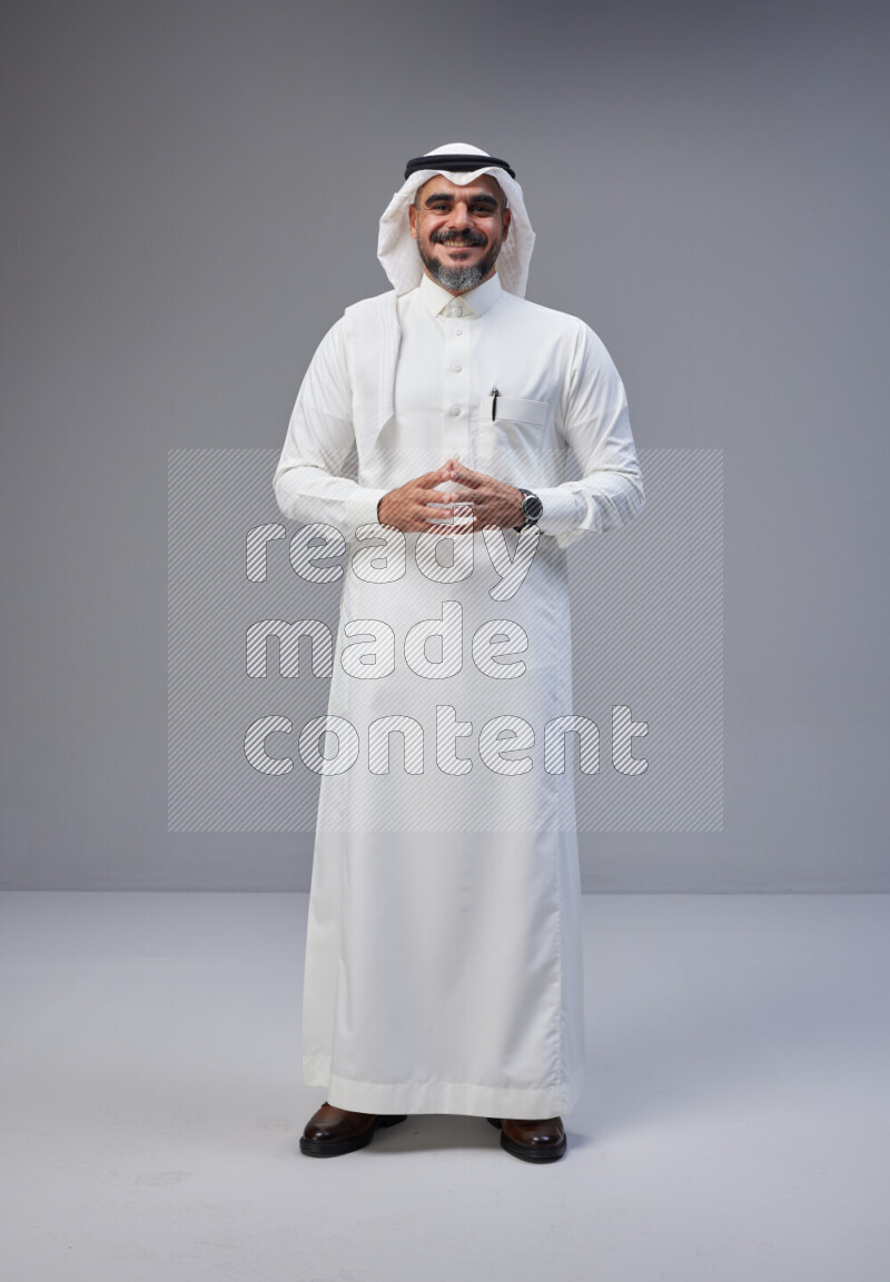 Saudi man Wearing Thob and white Shomag standing interacting with the camera on Gray background