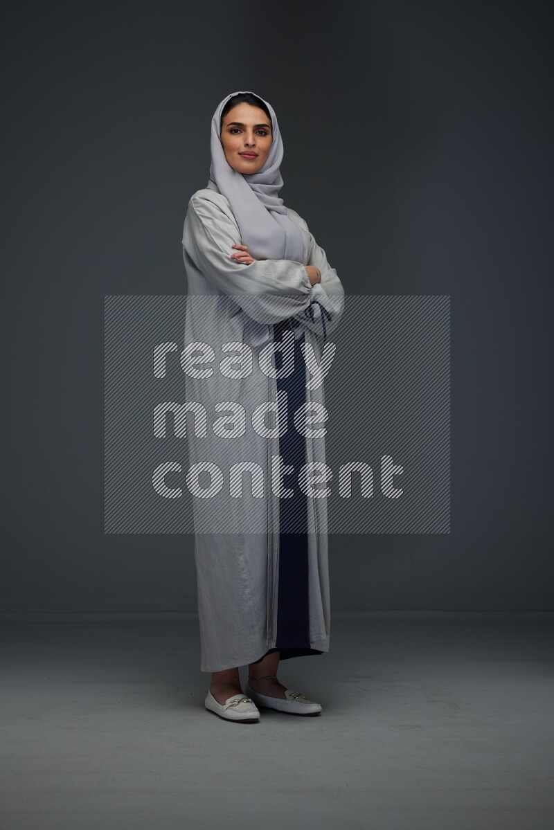 A Saudi woman wearing a light gray Abaya and head scarf standing and making multi poses eye level on a grey background