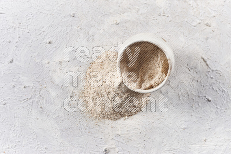A beige pottery bowl full of onion powder with fallen powder from it on white background