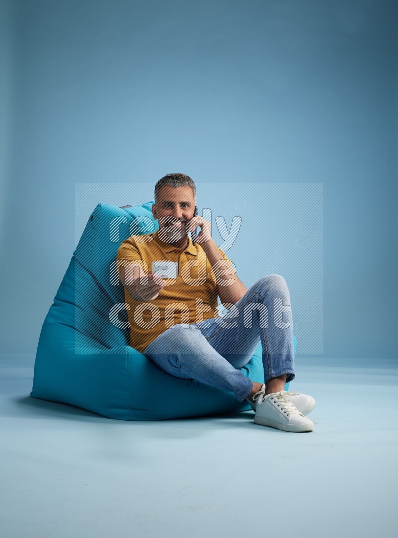 A man sitting on a blue beanbag and holding ATM card with phone