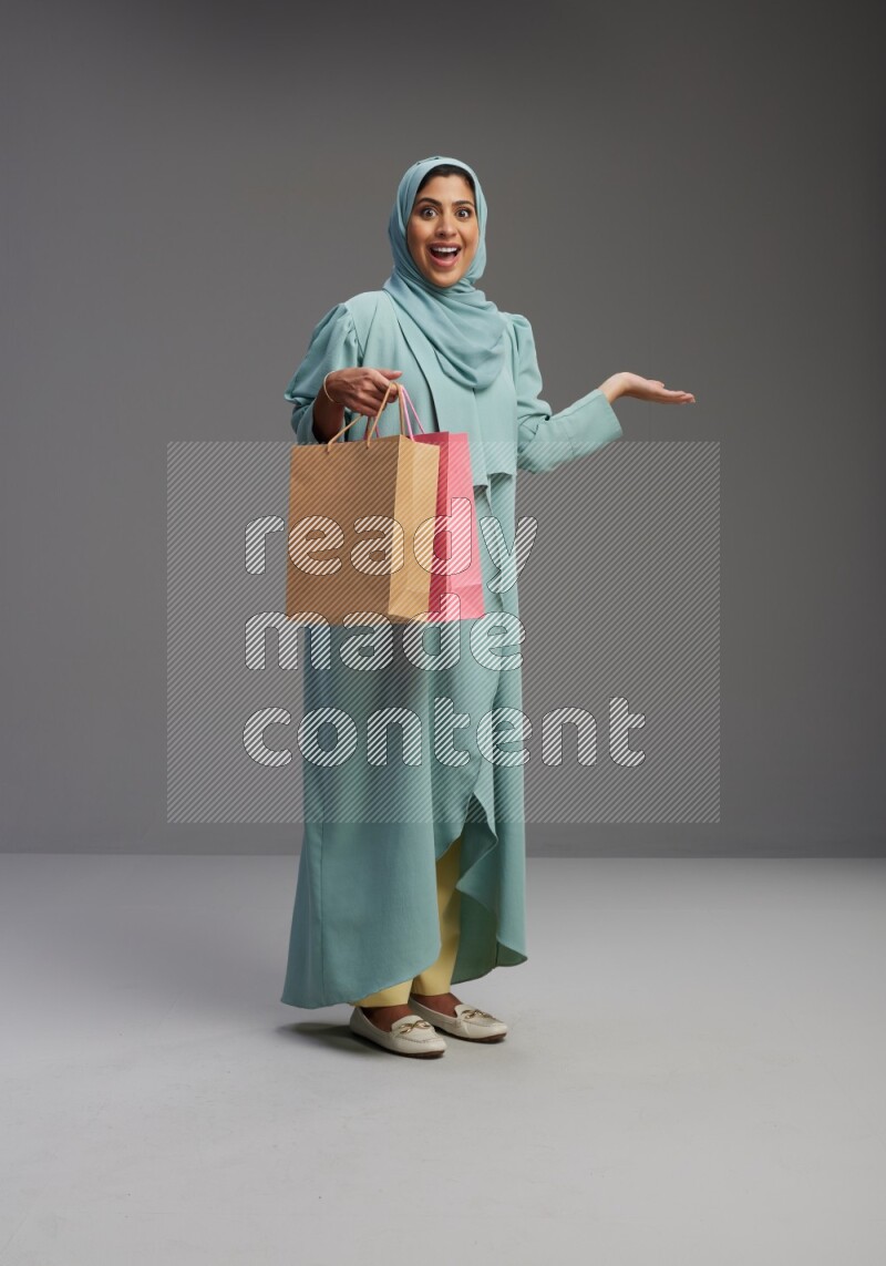 Saudi Woman wearing Abaya standing holding shopping bag on Gray background