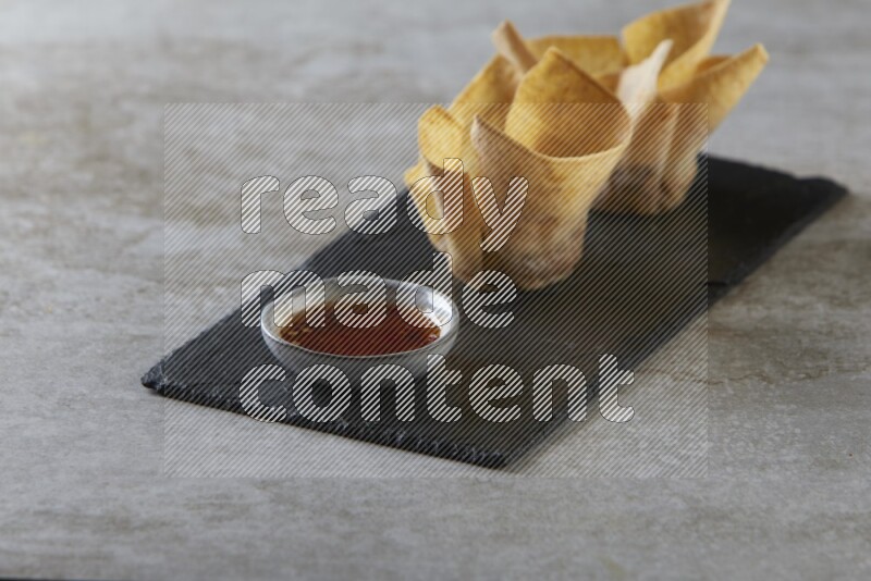 wonton cups with soy sauce ramkin on rectangle slate on grey textured counter top