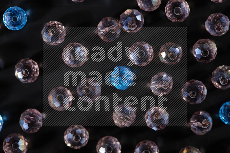 Rose and blue transparent crystal beads scattered on a black background