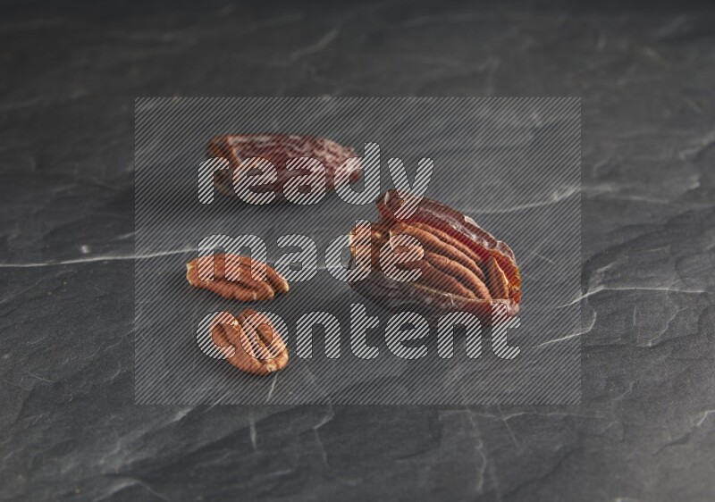 two pecan stuffed madjoul dates on a black textured background